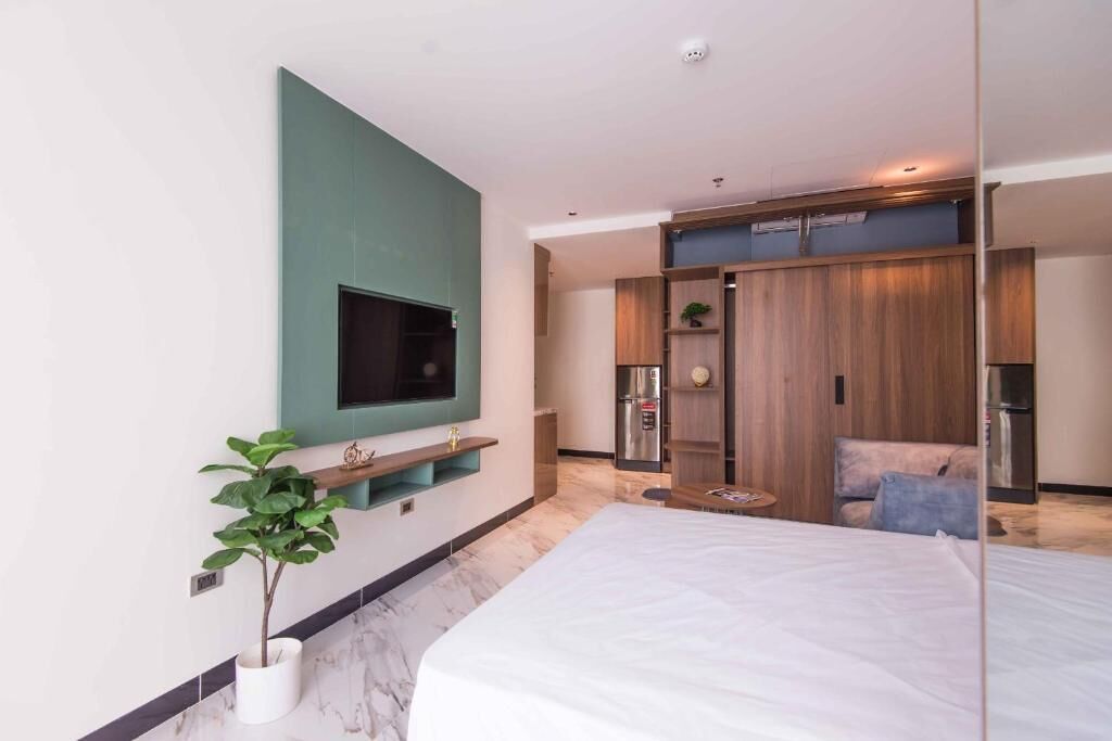 Een moderne slaapkamer met een groot bed, een aan de muur bevestigde televisie, een klein tafeltje en een kledingkast met inbouwplanken.
