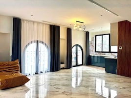 Um amplo hall de hotel com piso de mármore, grandes janelas com cortinas, um lustre moderno e vista para a cidade.