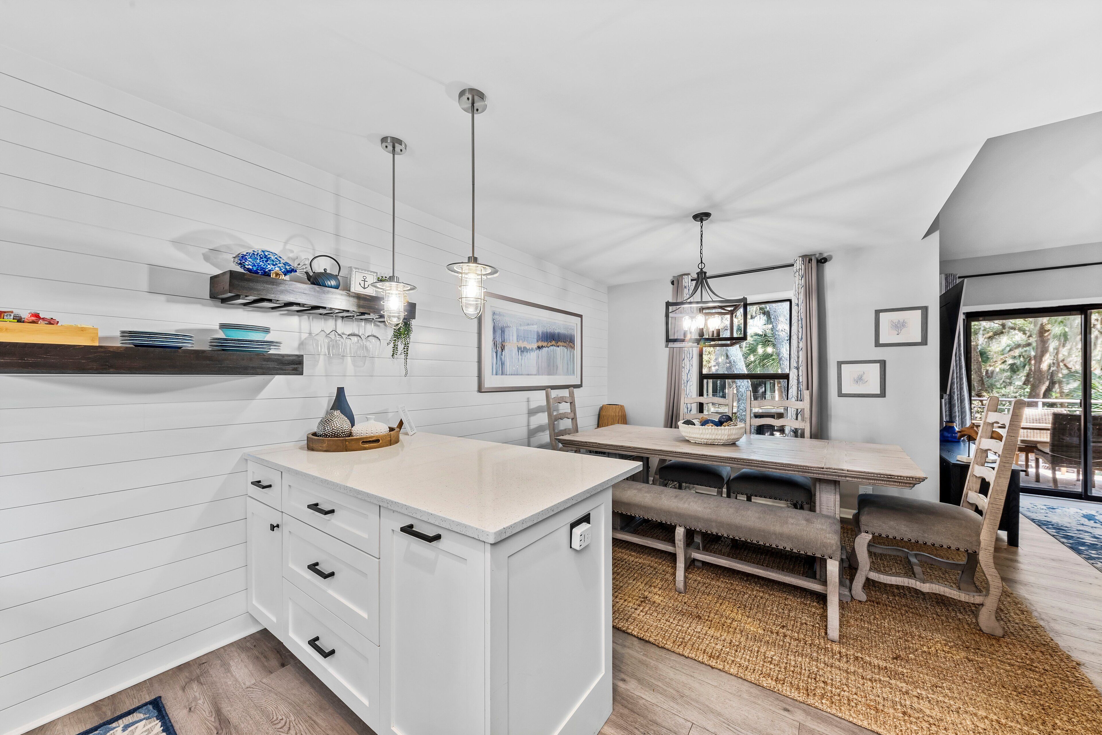 A modern kitchen with white cabinetry, a central island, pendant lighting, and a dining area with a bench and table.