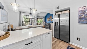 A modern kitchen with a large island, stainless steel appliances, and pendant lighting. - High Tide Hideaway by Sandpiper | Near Beach (Seabrook Island)