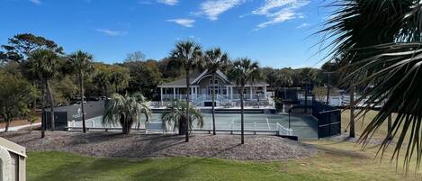 Un edificio grande con cancha de tenis techada, rodeado de palmeras y un área verde.