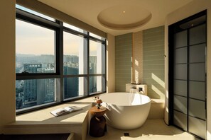 Un baño moderno con una bañera grande, una ventana con vistas a la ciudad y una mesita de madera con un florero.