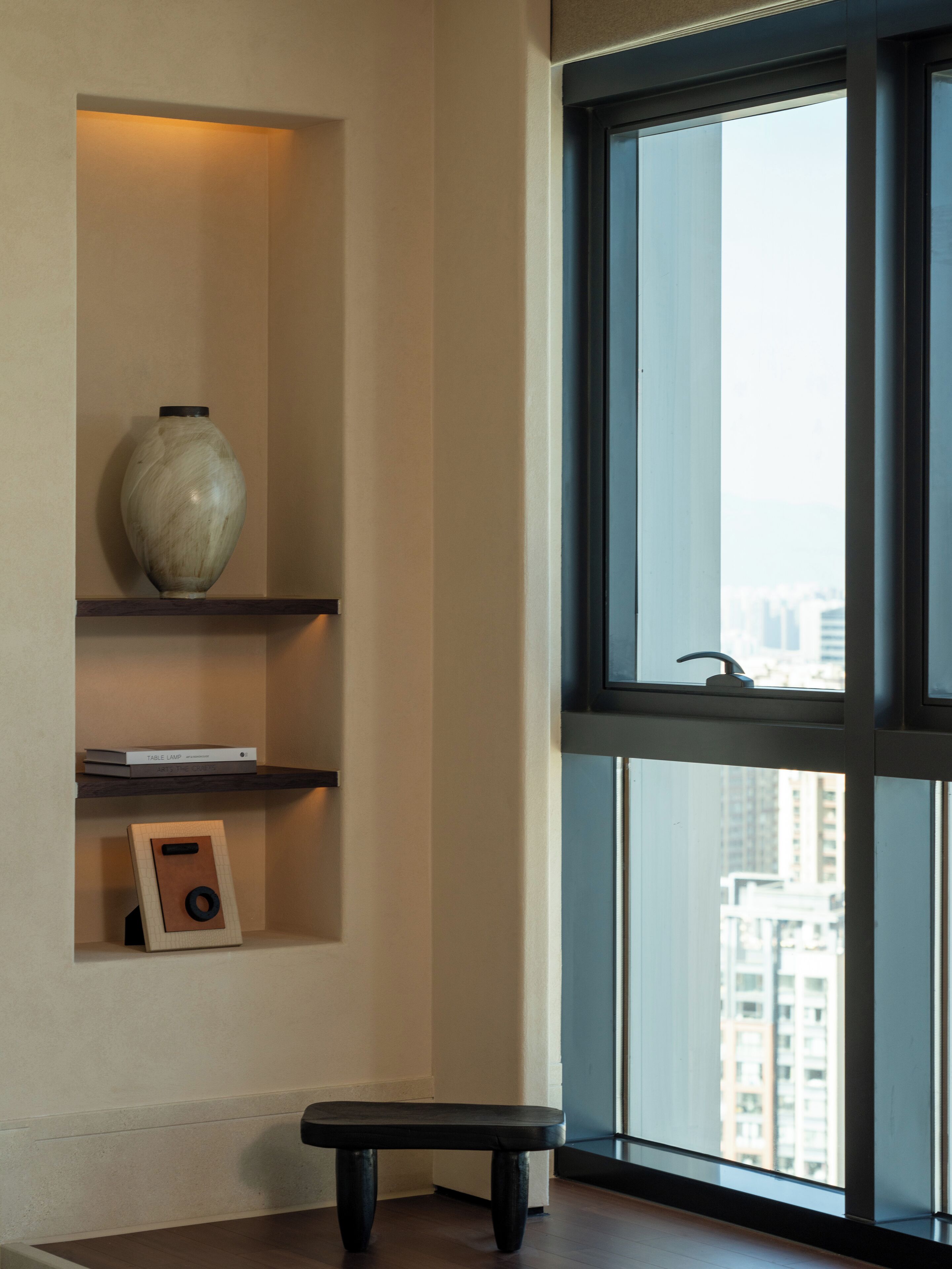 A modern interior with a large window, a vase, and a bench.