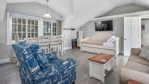 A spacious loft with a high ceiling, a dining area with a table and chairs, a sofa, a small wooden table, and a ceiling fan. - Cape Cod Magic at Starfish Cottage (South Yarmouth)