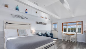 A bedroom with a bed, bedside tables, a desk, and chairs. There is a window with blinds and a view of the outside.