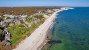 An aerial view of a coastal residential area with houses, a beach, and clear blue water.