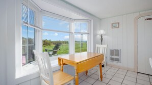A dining area with a wooden table and white chairs, large windows with blinds, a lamp, and a door with a 'NO SMOKING' sign.