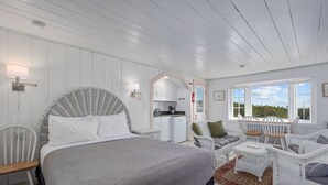 A room with a bed, a small kitchenette, a dining area with chairs, and a view through the window.