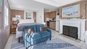 A bedroom with a bed, a blue sofa, a fireplace, and a kitchen in the background.