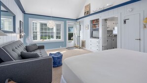 Un dormitorio con una cama grande, un sofá gris, un armario blanco y un televisor.