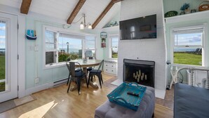 Una sala de estar acogedora con chimenea, un comedor con mesa y sillas, y vistas al mar a través de amplias ventanas.