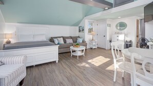 A bedroom with a bed, a sofa, a small table, and a chair. There is a window with a view of the outside.
