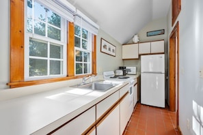 A compact kitchen with white cabinets, a stainless steel sink, a microwave, and a refrigerator. - Stay at The Salt Box - Steps from the Sea (South Yarmouth)