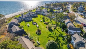 An aerial view of a coastal residential area with houses, lawns, and a beach.