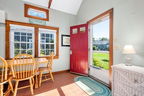 Ein Zimmer mit Esstisch, Stühlen, einer roten Tür und Blick auf ein Haus durch die Tür.