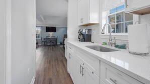 A modern kitchen with white cabinets, a built-in oven, a coffee maker, and a sink. - Summer Wind - Your Serene Cape Cod Getaway (South Yarmouth)