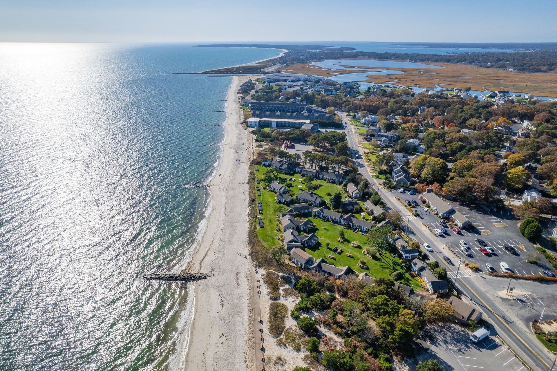 An aerial view of a coastal residential area with houses, a beach, and a road.