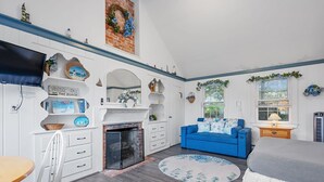 Un dormitorio con chimenea, un sofá azul, una cama con colcha gris y una alfombra redonda.