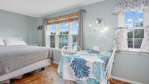 Une chambre avec deux lits, une table recouverte d’une nappe à motifs coralliens et une fenêtre agrémentée d’un rideau sur le thème de la marine.