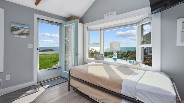 Een slaapkamer met een bed, een raam met uitzicht op zee en een deur naar buiten.