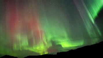 Ein Nachthimmel mit grüner Polarlichter über einer Berglandschaft.