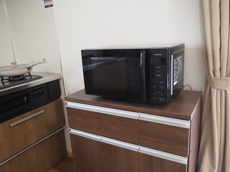 Una cocina compacta con microondas en un mueble de madera, una estufa con una olla y un refrigerador pequeño.