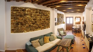 A cozy living room with a stone wall, a green sofa with patterned cushions, a wooden coffee table, and a dining area with a wooden table and chairs.
