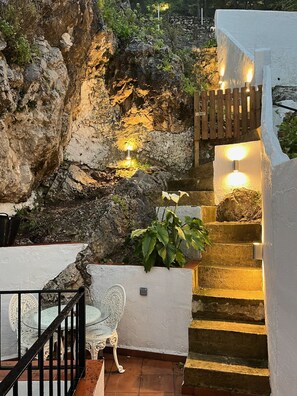 Una escalera de piedra con barandilla blanca, una pared blanca con una planta en maceta y una silla decorativa.