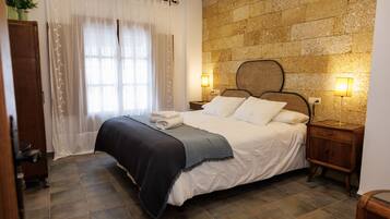 A bedroom with a bed, two bedside tables with lamps, a wooden headboard, and a stone wall.