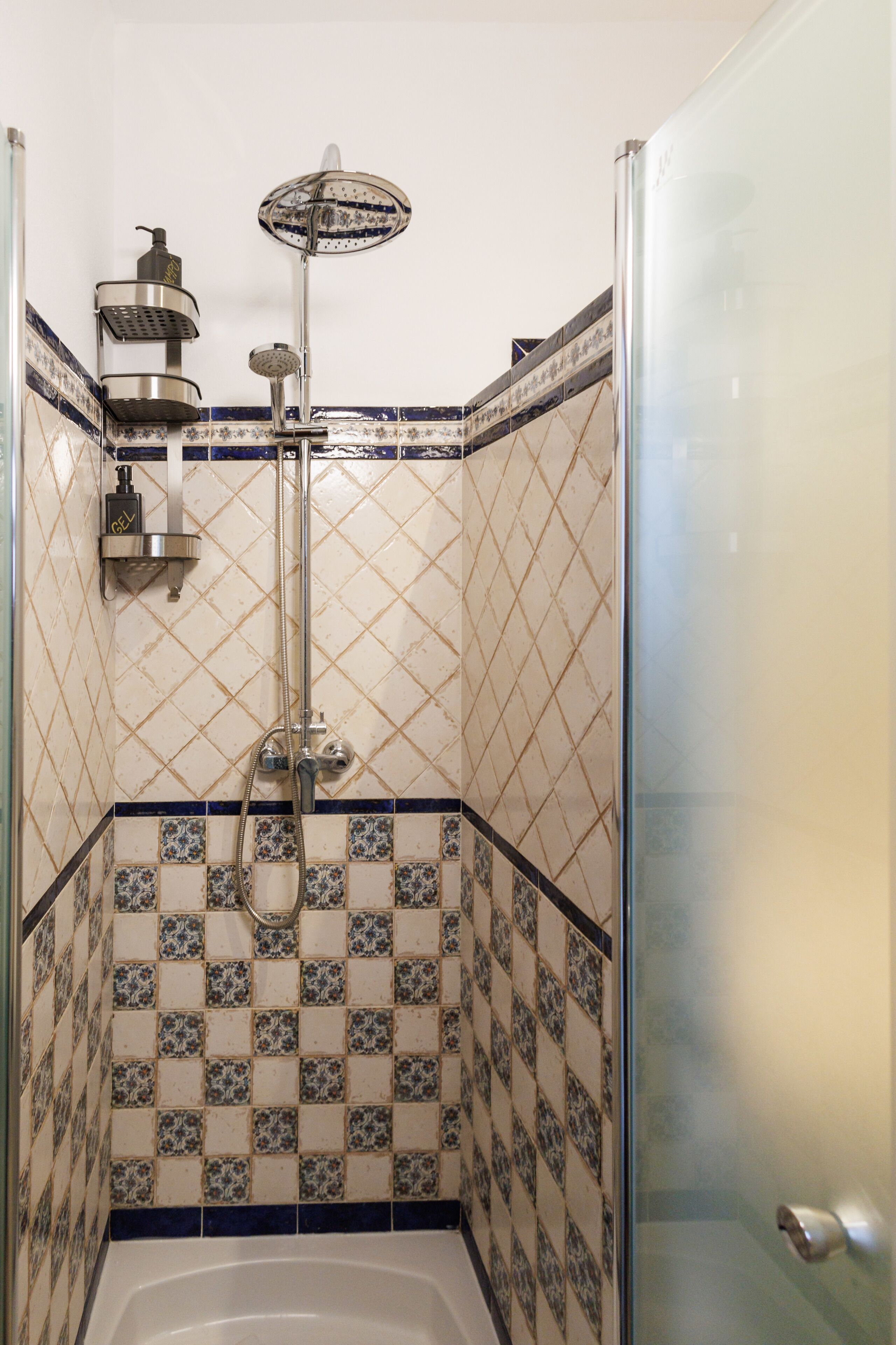 A shower area with a glass door, a handheld showerhead, and a wall-mounted faucet.