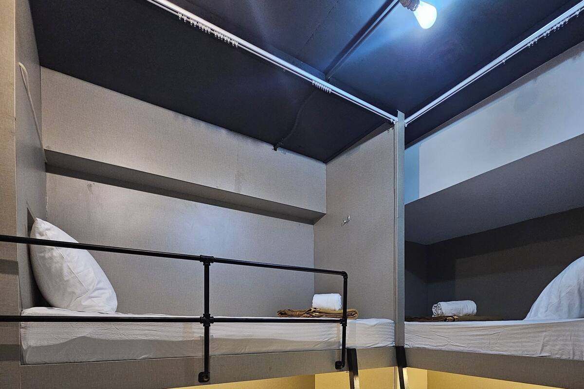 A bunk bed room with a ladder, white bedding, and a light fixture on the ceiling.