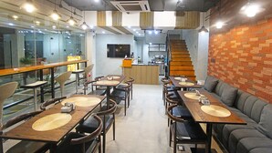 Un restaurante moderno con mesas y sillas de madera, un muro de acento de ladrillo y una escalera que lleva a una zona de cocina.