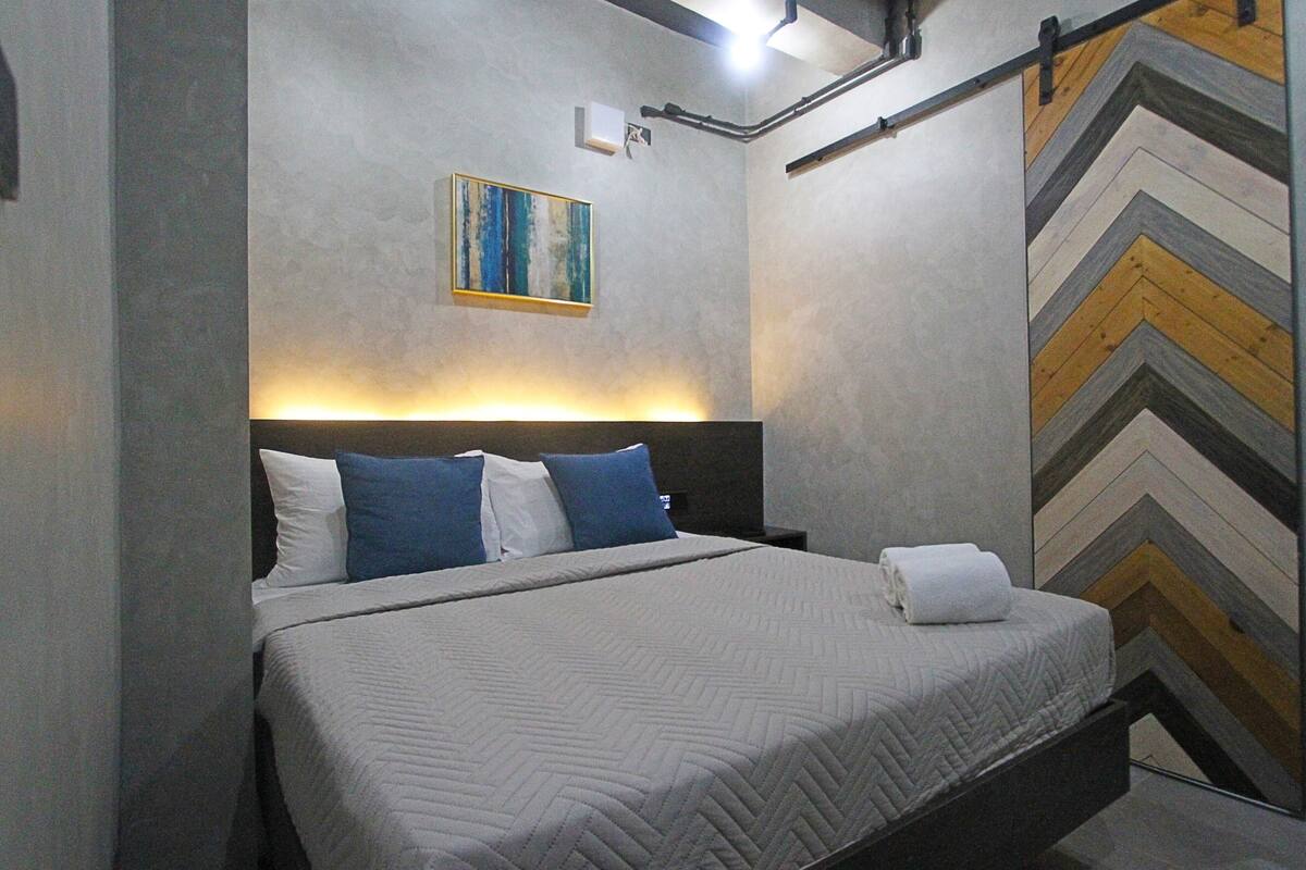 A modern bedroom with a bed, a headboard, a painting, and a chevron-patterned wall.
