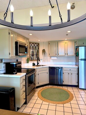 A kitchen with white cabinets, stainless steel appliances, a microwave, oven, dishwasher, and a green rug.