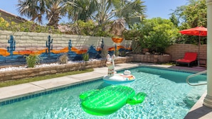A swimming pool with inflatable toys, a mural on the wall, and a red umbrella.