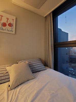 Ein Hotelzimmer mit einem Bett, gestreiften Kissen, einem Wandbild und einem großen Fenster mit Blick auf die Stadt.