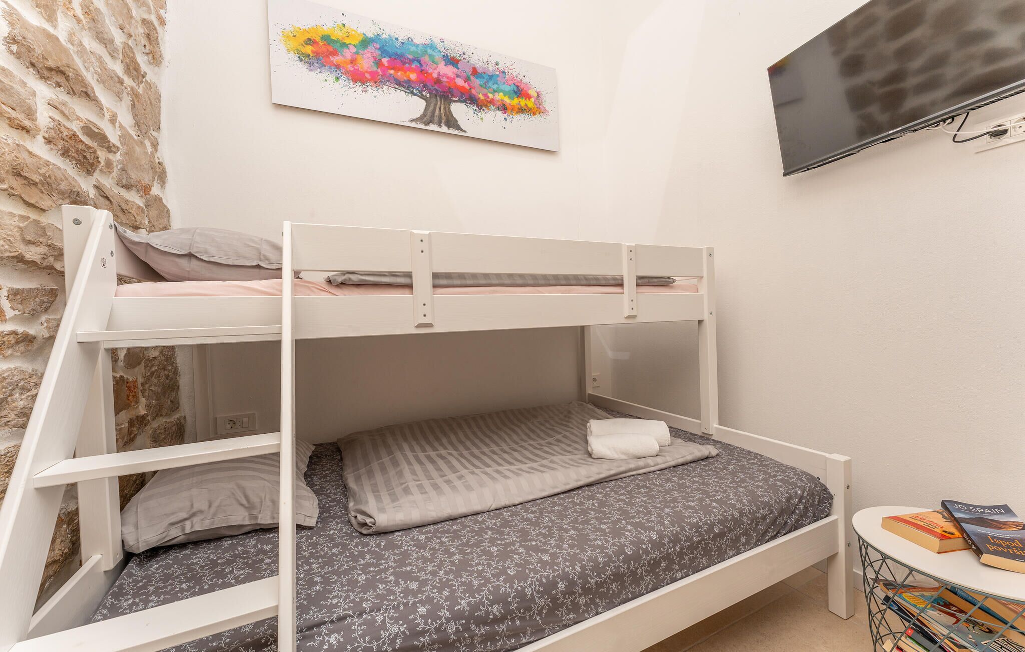 A bunk bed room with a stone wall, a painting of a tree, and a TV mounted on the wall.