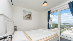 Un dormitorio con cama, un cuadro, una ventana con cortinas y vistas al exterior.