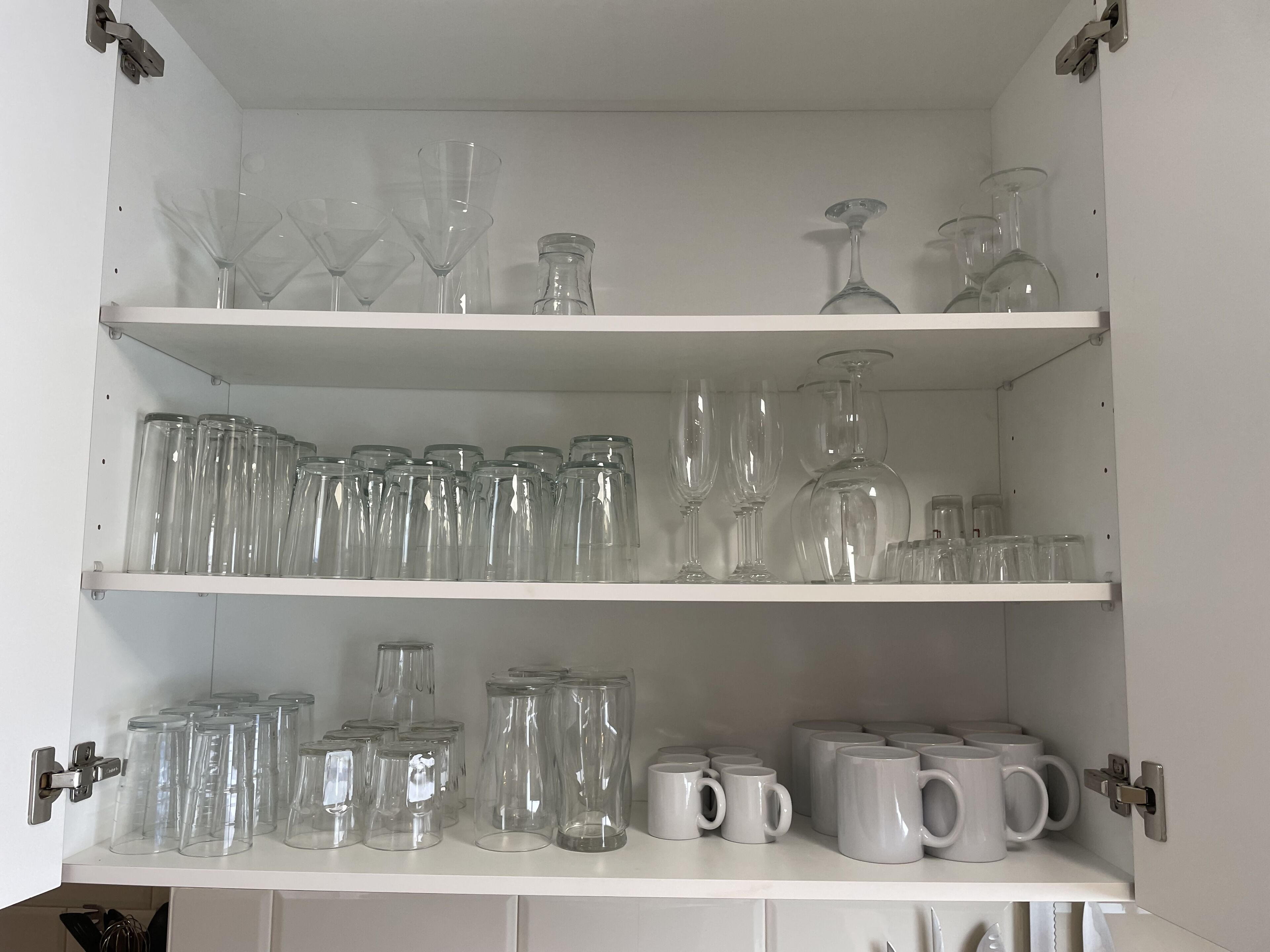 Ein weißes Schrank mit drei Regalen, gefüllt mit verschiedenen Gläsern und Tassen.