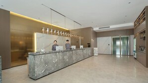 Una zona de recepción moderna con una barra de mármol, dos recepcionistas, un muro de cristal y un ascensor.