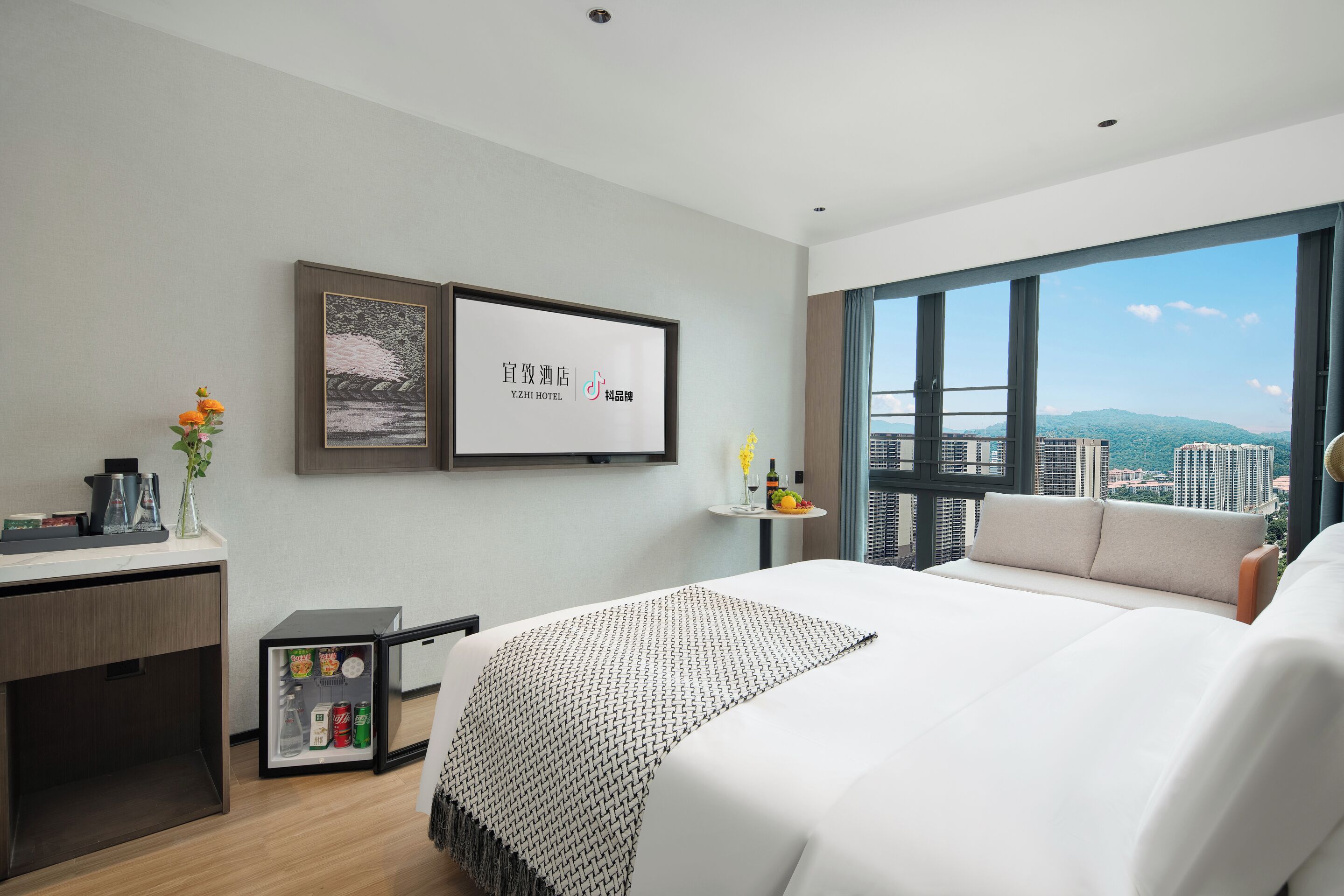 Een moderne hotelkamer met een groot bed, een klein bureau, een minibar en uitzicht over de stad.