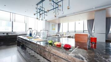 Une cuisine d’hôtel moderne, dotée d’un plan de travail en marbre, d’un buffet et de grandes fenêtres.