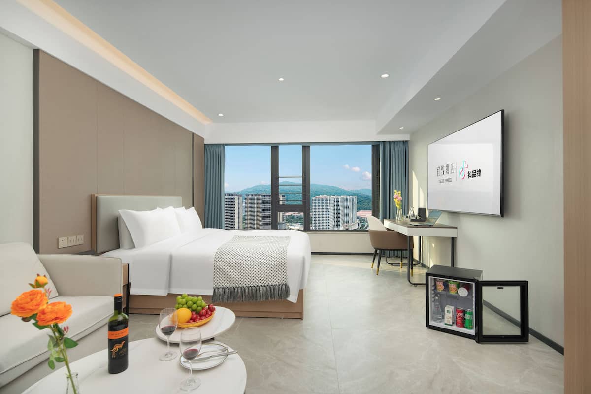 Habitación de hotel moderna con cama, escritorio, televisión y vistas a la ciudad.