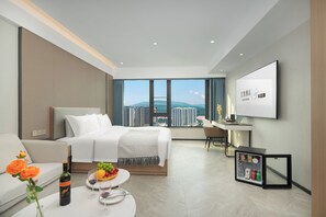 Ein modernes Hotelzimmer mit Bett, Schreibtisch, Fernseher und Blick auf die Stadt.