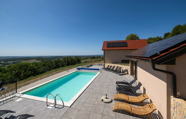 A swimming pool with a view of the countryside, a building with solar panels, and outdoor seating.