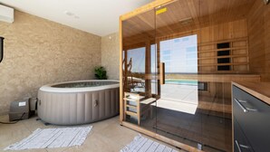 A modern spa room with a hot tub, wooden sauna, and a glass-enclosed area with a view of the outdoors. - Luxurious home in Kamesnica with sauna (Kamesnica)