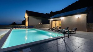 A swimming pool with lounge chairs and a covered area, surrounded by stone walls and a view of the landscape. - Luxurious home in Kamesnica with sauna (Kamesnica)