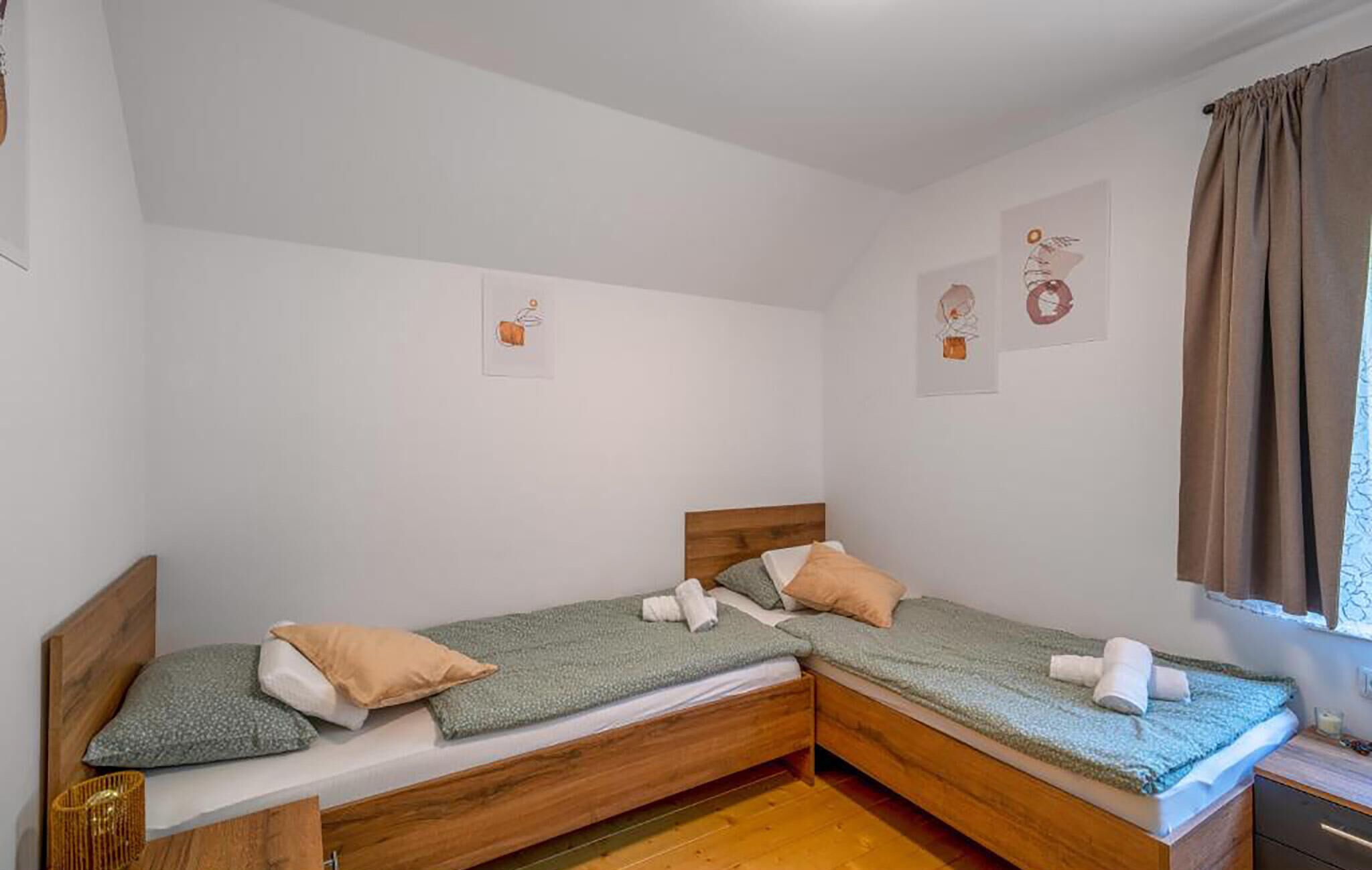 A room with two wooden beds, a small bedside table, and a window with curtains.