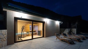 A modern building with a glass door entrance, a pool area with lounge chairs, and a stone wall. - Luxurious home in Kamesnica with sauna (Kamesnica)