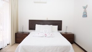 Habitación de hotel con una cama grande, dos mesitas de noche, aire acondicionado instalado en la pared y un letrero decorativo.